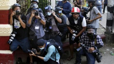 Photojournalists take cover near the entrance of a monastery where military supporters gathered to attack protesters and media in Yangon on February 18, 2021 (EPA-EFE)
